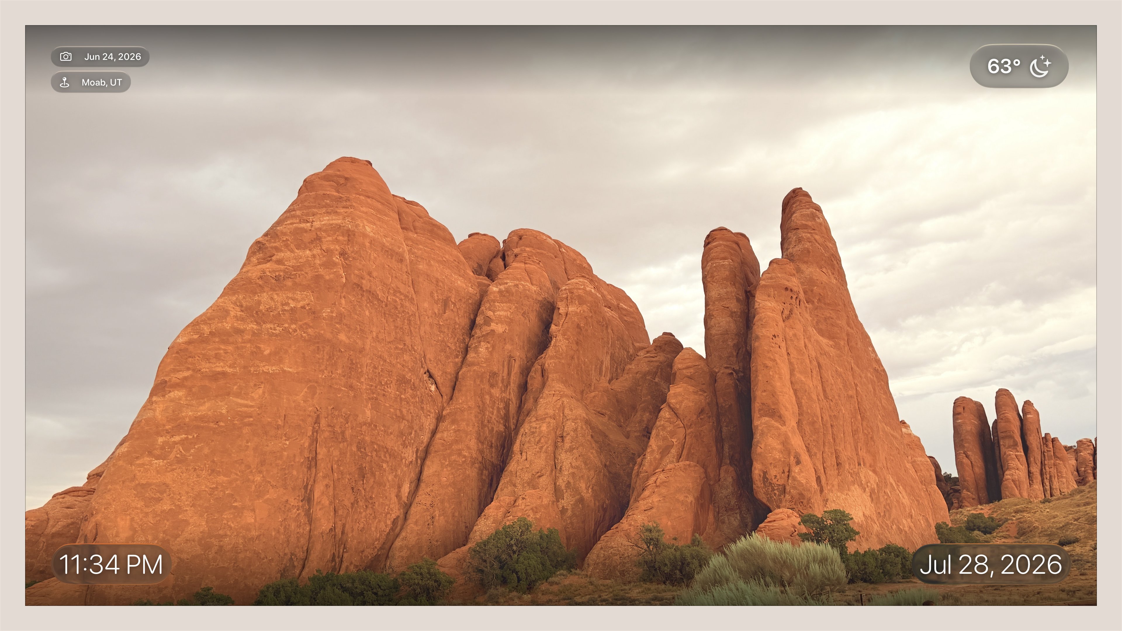 Apple TV showing full-screen photo of red rock formations with time, date, location, and weather chip